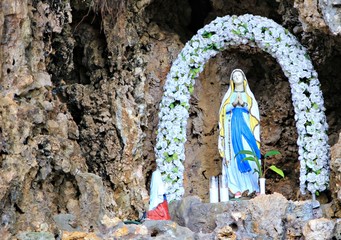 Grotto with a statue of the Blessed Virgin Mary The statue of the Blessed Virgin Mary with an arch of roses in a grotto 