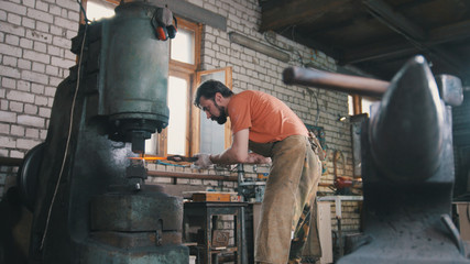 Man blacksmith forges the metal at the mechanical hammer