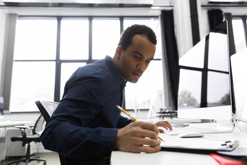 Wall Mural - Afro american businessman making notes while sitting at his desk