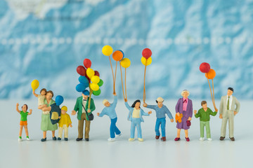 Wall Mural - Miniature people with family holding balloons with blue map in the background as happy family or travel concept