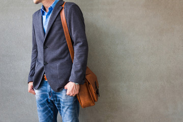 Businessman with casual suit outfits and leather bag standing over gray grunge background with space, travel and fashion concept