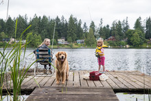 Two Kids And A Dog Sitting On A Dock Fishing In A Lake