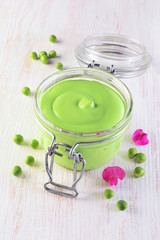 Healthy food. Fresh puree of green peas in open glass jar with pink flowers of sweet pea