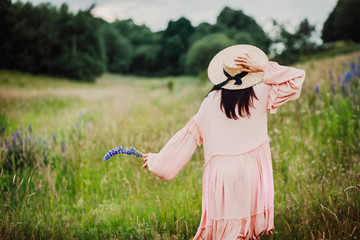 Woman in pink dress and hay hat walks on the green field