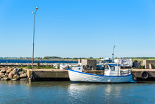 Small White And Blue Fishing Boat Moored At Concrete Pier In Open Coastal Landscape.