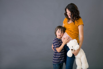 Wall Mural - Little child, boy, hugging his pregnant mother at home, isolated image