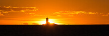 Silhouette Of A Lighthouse Against The Background Of An Orange Sky At Sunset. With Glowing.