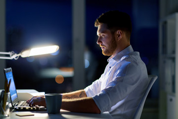 man with laptop and coffee working at night office