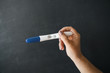 © galaganov - Pregnancy test in a girl's hand, against a black chalkboard background. The concept of pregnancy.