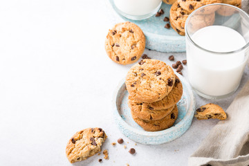 Stack of chocolate chip cookies on blue stone plate with glass of milk on light gray background. Selective focus. Copy space.