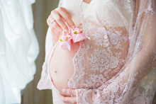 Pregnant Woman Holding Pink Baby Shoes On Her Belly