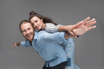 Wall Mural - Happy young couple piggybacking and smiling at camera isolated on grey