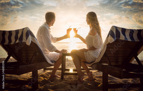 Fotografering Paar mit Cocktails am Strand auf Strandliegen schaut den Sonnenuntergang im Urla