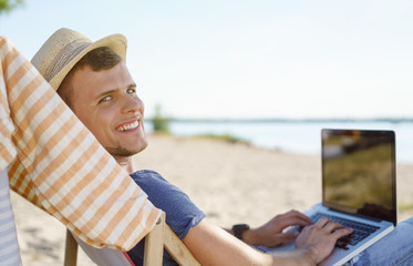 Attractive young man relaxing at the beach with laptop