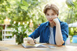 Girl preparing for exam. Outdoor portrait of a confident young woman writing in notepad and looking at camera preparing for her study or work. Soon to become a scriptwriter.