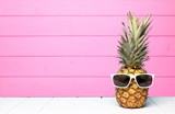 Hipster pineapple with sunglasses against a pink wooden background
