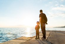 Father And Son Looking At The Sea At Sunset
