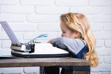 writer kid sitting at table and typing typewriter with paper