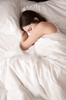© fizkes - Tired young woman sleeping well on the side in bed with white sheets, resting after sleepless night. Female student lying in bed until late morning. Getting enough sleep concept. View from above