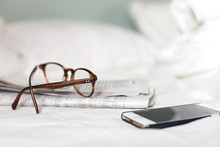 Glasses, Newspaper And Phone On White Sheets