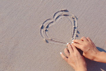 Wall Mural - Female hand drawing heart symbol on white sand beach