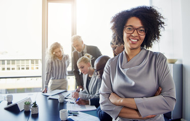 Wall Mural - Confident young businesswoman with coworkers talking in the background