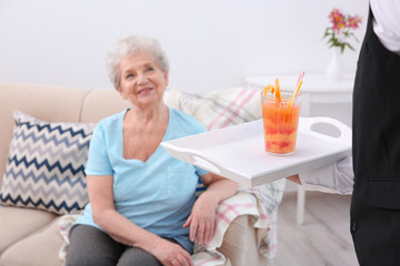 Wall Mural - Young man serving glass of juice for elderly woman. Concept of nursing