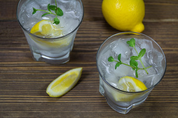 Refreshing beverage with lemon, ice and mint leaves in glasses, isolated on wooden background