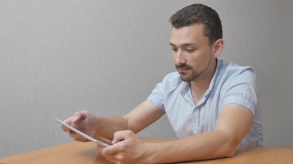 The happy man in amazement uses a tablet. Someone is happily using the device to satisfy themselves