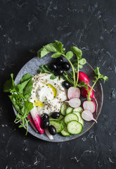 Wall Mural - Healthy diet snack in a mediterranean style - greek yogurt, radishes, olives, cucumbers, lettuce on dark background, top view. Flat lay. Copy space