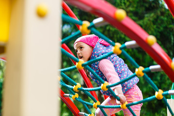 Portrait of Happy little blond girl playing on a rope web playground outdoor