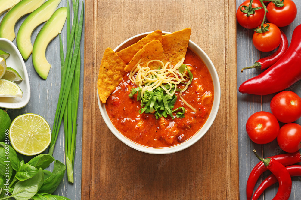 Bowl with delicious chili turkey on wooden board