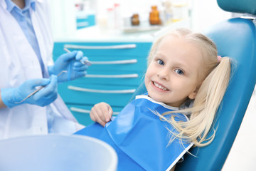 Dentist examining little girl's teeth in clinic