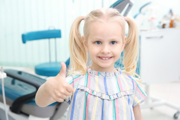 Wall Mural - Cute little girl showing thumb up sign at dentist's office