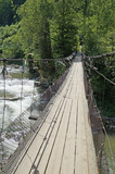 Fototapeta Mosty linowy / wiszący - Suspension bridge across the mountain river swaying from the wind. Bridge over the river