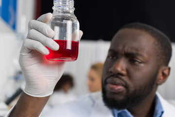 African American Scientist Examine Flask With Red Luquid Working In Modern Laboratory, Male Researcher Making Experiment In Lab