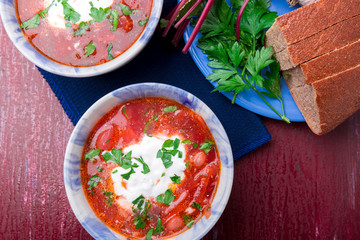 Ukrainian traditional borsch. Russian vegetarian red soup  in blue bowl on red wooden background.  Borscht, borshch with beet. Two plates. Top view.