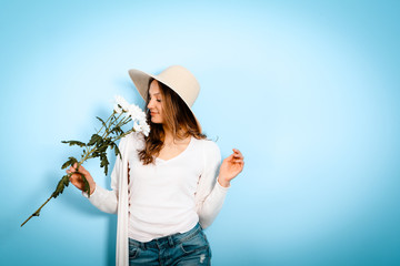 young beautiful woman sniffing a flower on blue background indoor