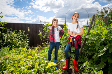 Two young sisters working at backyard garden at sunny day