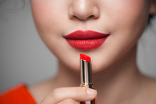Close Up Portrait Of Attractive Girl Holding Red Lipstick Over Grey Background