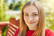 © sementsova321 - Close up portrait of cute female having blue piercing eyes, curling eyelashes, glowing face with dimples and fair hair sitting at bench against green park background enjoying fresh air outdoors