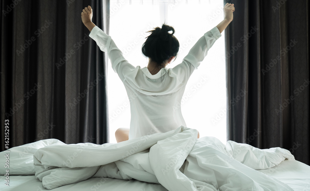 Asian women wake up from sleep. are  stretch herself  in the morning on the weekend sit on the bed at luxury room in Relax and weekend concept. - obrazy, fototapety, plakaty 