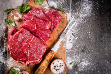 Wall Mural - Meat. Beef, veal. Fresh raw tenderloin, piece without bone. For frying grilling barbecue. Cut into steaks, whole. On black stone table,cutting board, spices, salt, fork for meat. Top view copy space