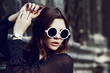 © Victoria Fox - Outdoor close up portrait of young beautiful girl posing in street. Model looking down, wearing stylish white round sunglasses, wrist watch, polka dot blouse. City lifestyle. Female fashion concept