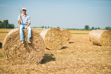 Smiling Farmer Sitting On An Hay Bale In His Field