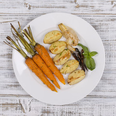 Young potatoes, carrots, onions, peppers, garlic baked in the oven on the white plate. Top view