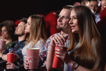 Attractive young woman smiling cuddling with her boyfriend while watching a movie together at the cinema dating love romance relationships people lifestyle entertainment leisure weekend concept.