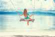 Young woman with long blond hair swinging on a swing on the shore of the tropical sea