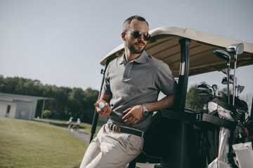 Wall Mural - Stylish golfer holding golf ball and looking away while leaning on golf cart