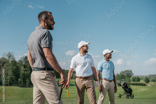 Fotografie, Obraz young multiethnic golf players looking away while standing on pitch